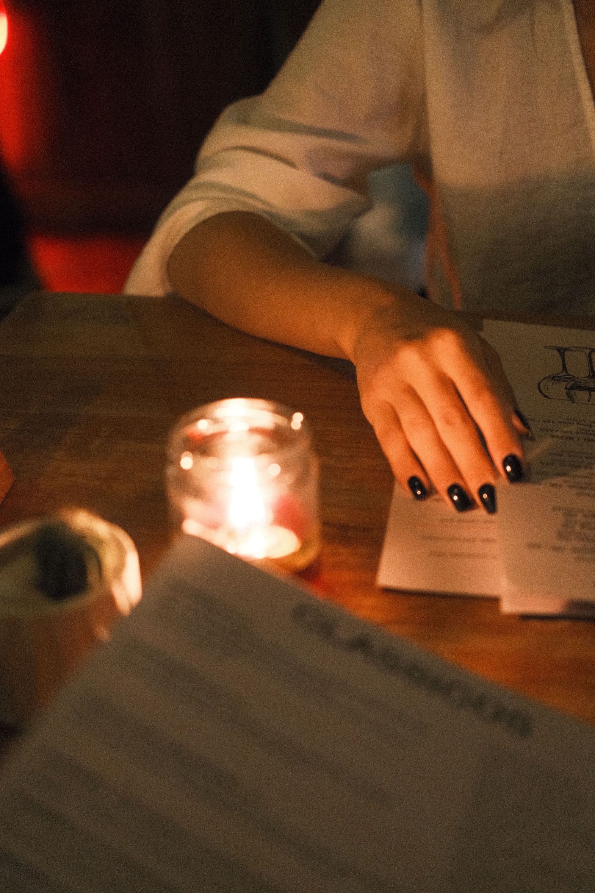 A hand resting on a table beside a candle and a page of notes